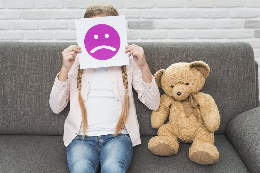 close-up-girl-sitting-with-teddybear-holding-sad-face-emoticons-paper-front-her-face (1).jpeg